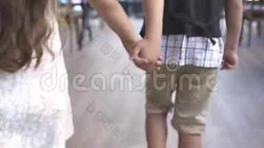 小男孩和小女孩牵着手走在咖啡馆里。 小男孩抱着小女孩走着
